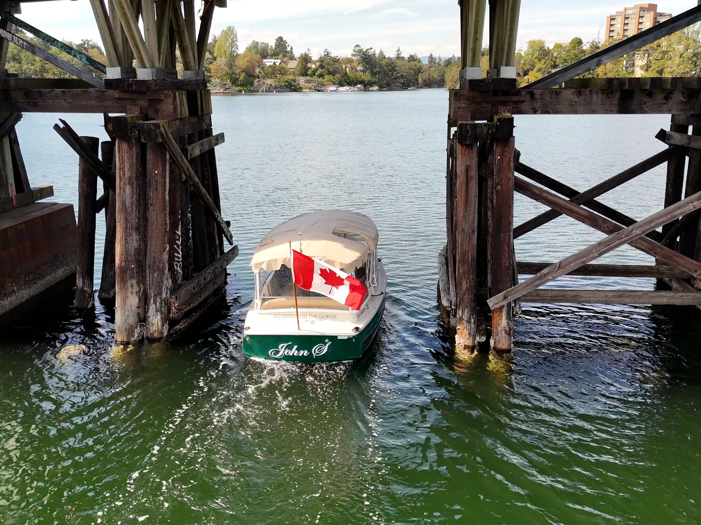 Boat with Canadian flag under wooden bridge on a sunny day.